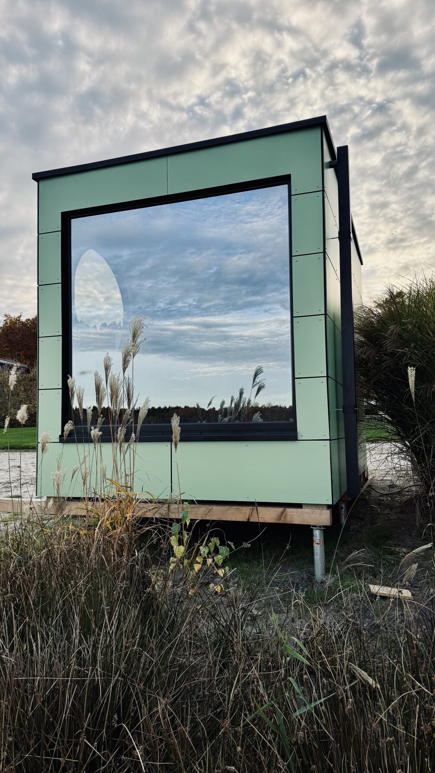 Außenansicht der grünen Design-Gartensauna mit Bullauge von PLUSGRAD