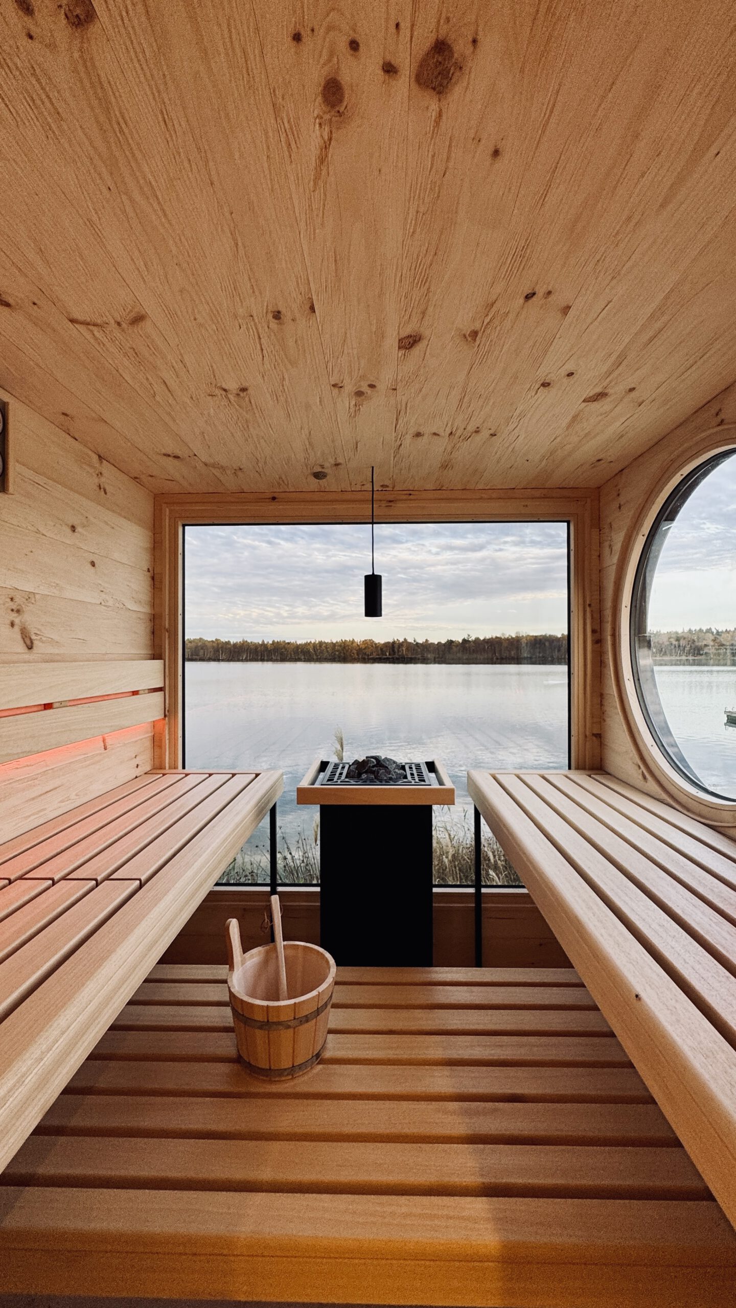 Innenansicht der Gartensauna mit Bullauge und Blick auf den See – PLUSGRAD Saunakonzept
