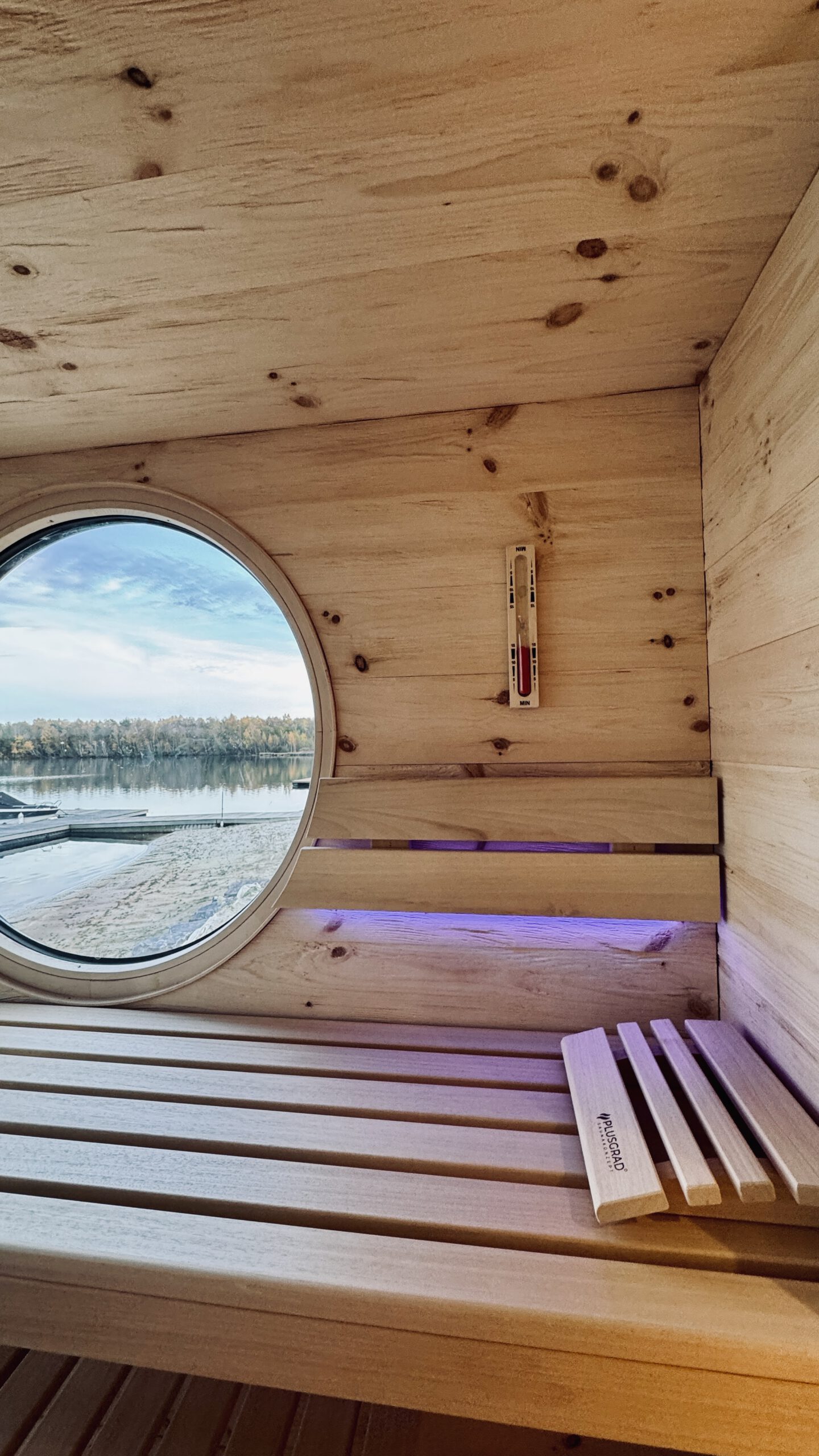 Innenansicht der Gartensauna mit Bullauge und Blick auf den See – PLUSGRAD Saunakonzept