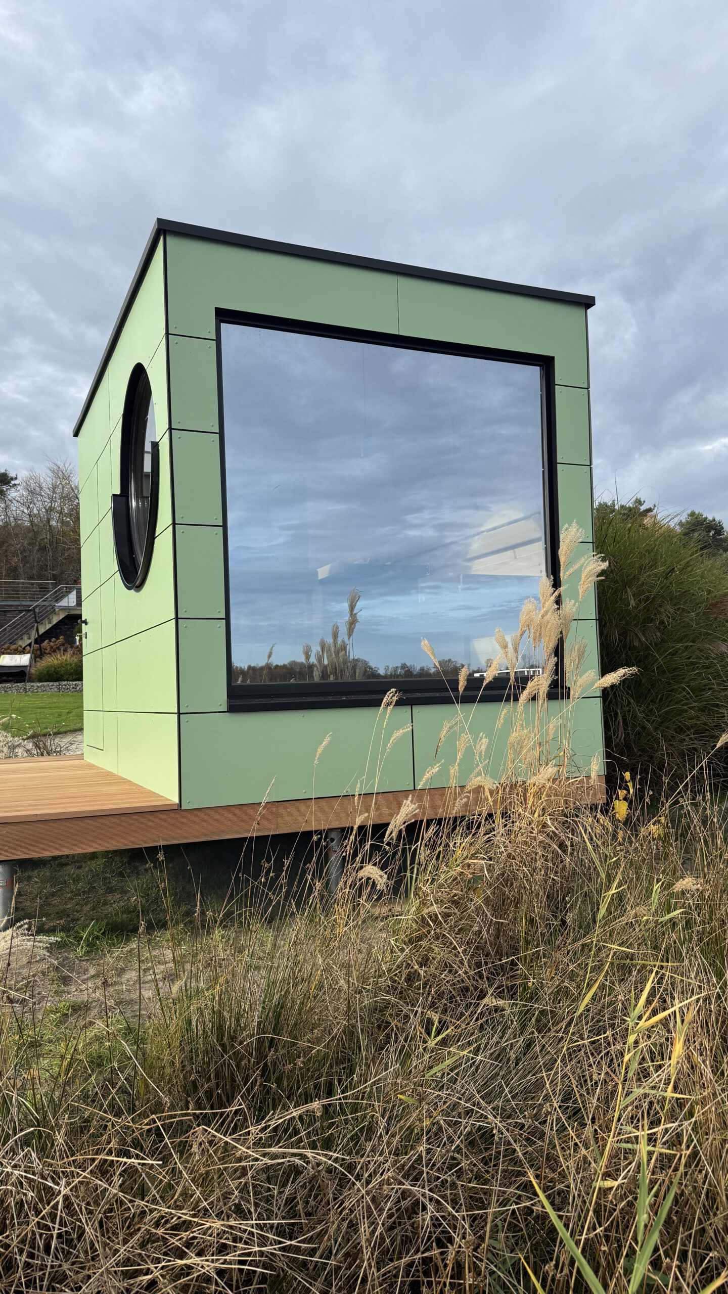 Außenansicht der grünen Design-Gartensauna mit Bullauge von PLUSGRAD